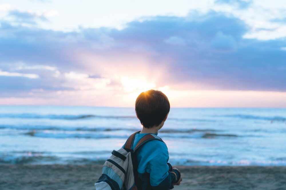海岸に沈む夕日を見つめる男の子の背中。もう戻れない幼い記憶を思い出してエモい気持ちになる。