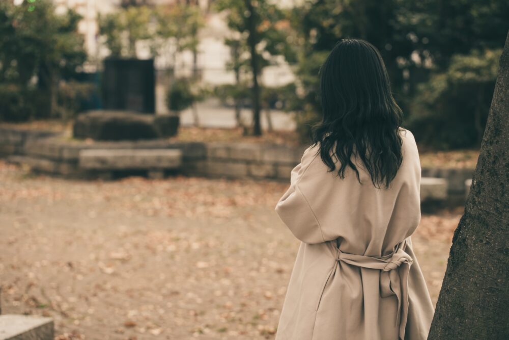 公園で切なげにたたずむ女性の背中。中国語のemoでネガティブな感情を表現する。