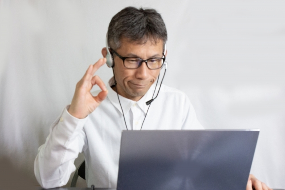 ヘッドセットをしてノートパソコンに向かってOKサインをする男性。ポイントを押さえれば失敗なく中国語オンラインレッスンが選べる。