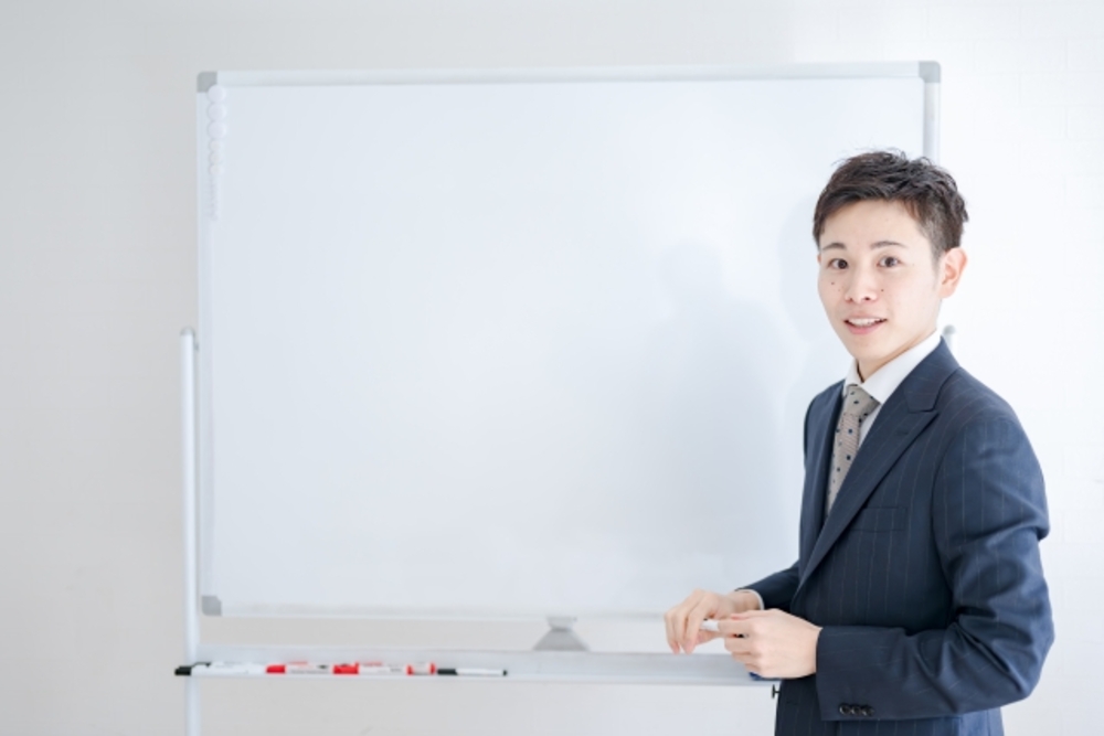 ホワイトボードに向かって解説する中国語教師。中国語検定とHSKのどちらを受けるべきかを解説する。