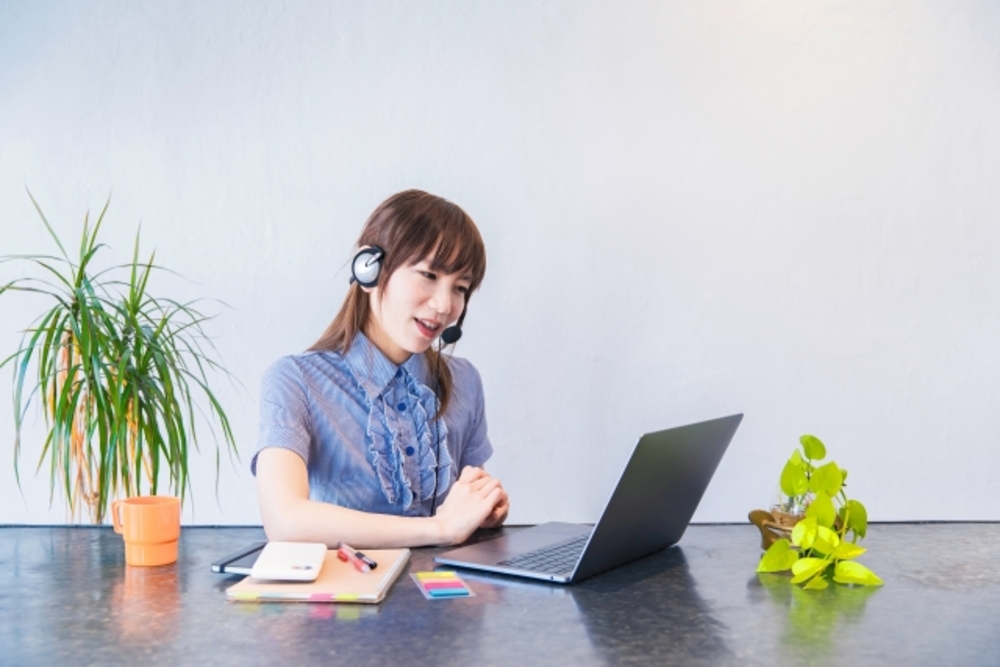 ヘッドセットを付け、脇にはメモを置いてノートパソコンに向かう女性。中国語オンラインレッスンで効果的な学習をする。