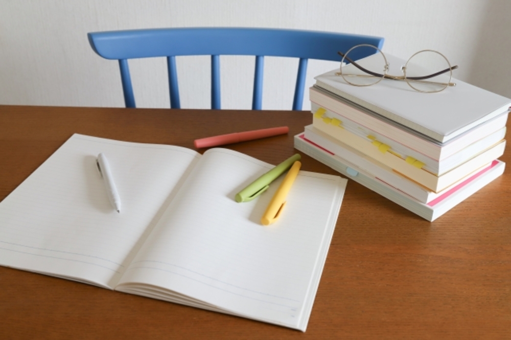 ノートと4色のペン、積み上げた参考書がテーブルに並ぶ。中国語の独学の準備ができた机の上。