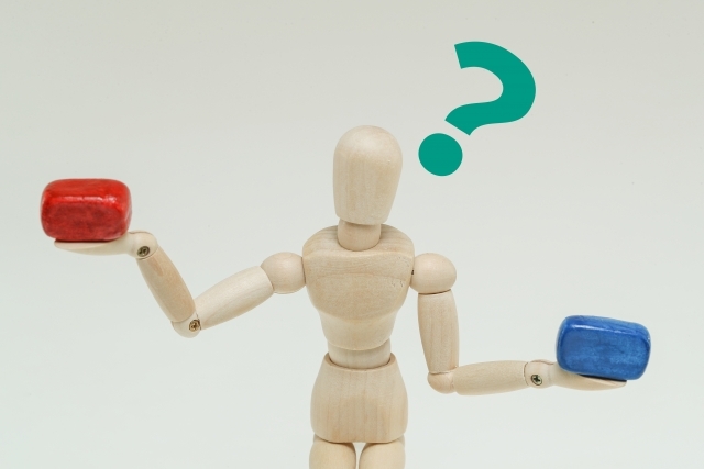 赤と青のブロックを両手に持って首を傾げる木製の人形。中国語検定とHSKの違いを比較する。