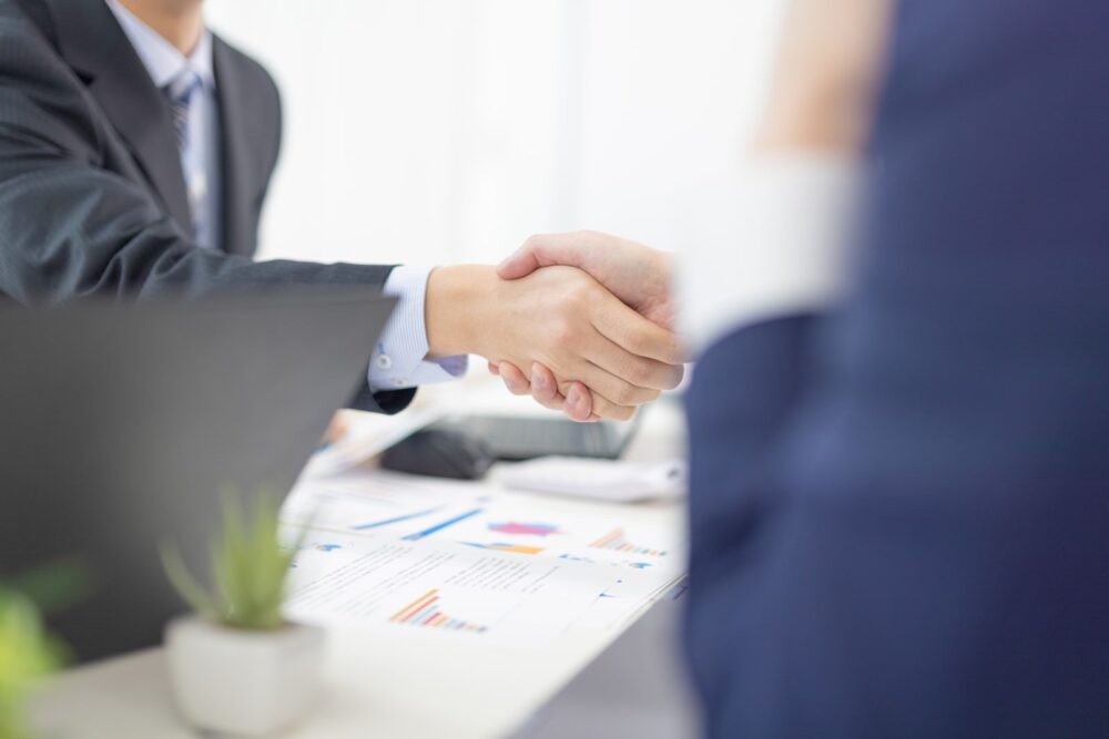 ビジネスシーンで握手をしている男性2人。ちょっとした中国語の挨拶から交流が生まれる。