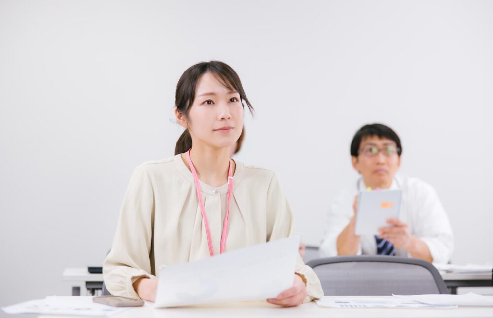 会議室で資料を持ちながら真剣に話を聞く女性。中国語を活かした仕事に就くためには真剣な努力が必要。