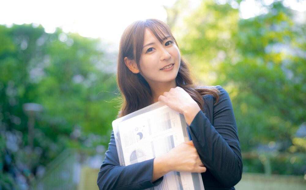 新緑をバックに微笑むスーツ姿の女性。朝一番に出会ったときに中国語の挨拶を使ってみる。