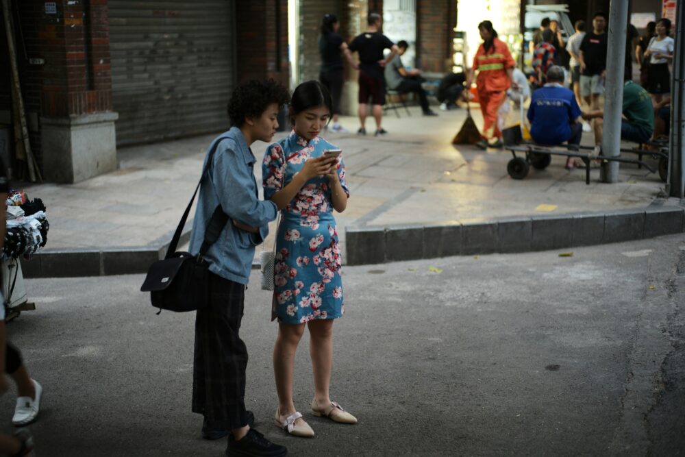 街角でスマホを見ながら会話している中華圏の女性2人。