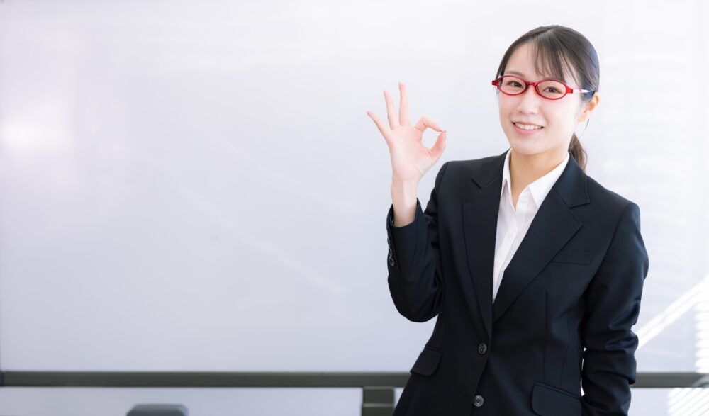 ホワイトボードの前でOKポーズをする女性講師。中国語検定に向いている人の特徴を解説する。