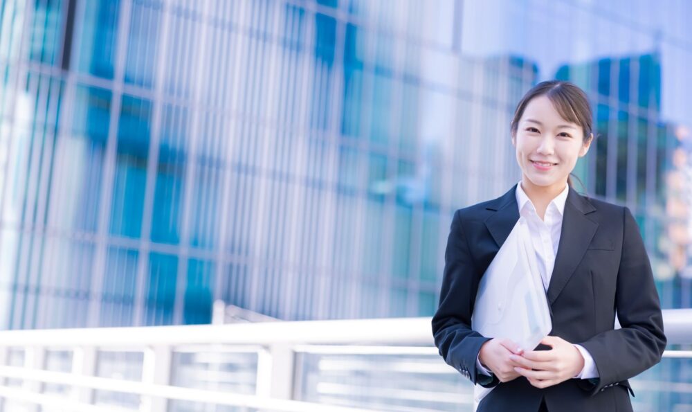 スーツを着てファイルを持った女性がほほ笑んでいる。転職エージェントを活用すれば、中国語を活かした仕事を見つけるためのサポートが受けられる。
